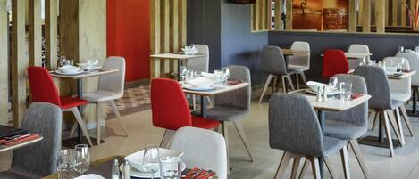 Un restaurant moderne avec des éléments décoratifs en bois, des chaises grises et rouges, et des tables dressées pour le repas.