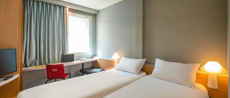 A hotel room with two beds, a desk with a laptop, a chair, a TV, and a window with curtains.
