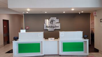 Een receptiebalie met twee loketten, een bordje met de tekst 'Holiday Inn' en een camera aan het plafond.