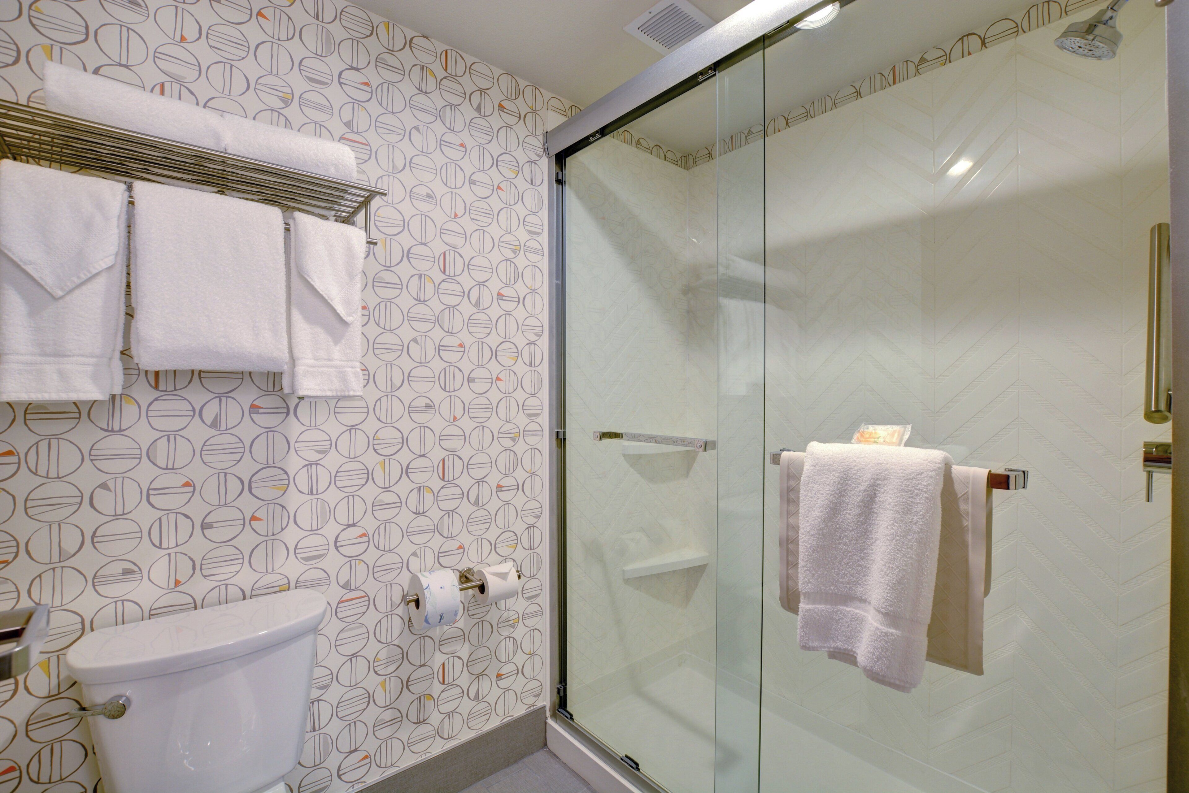 Une salle de bain avec des toilettes, une douche en verre et un mur décoré d’un motif.