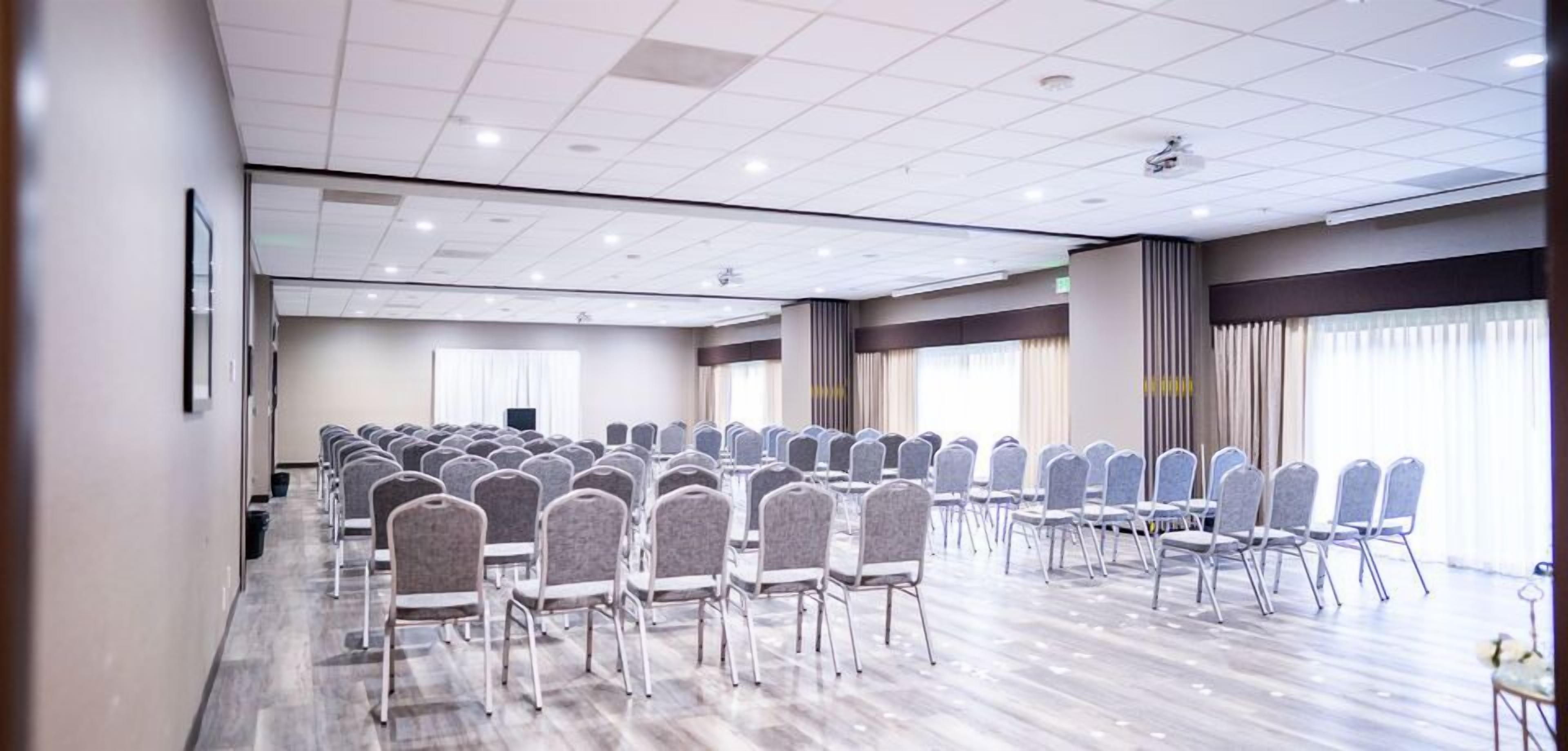 Un salón de conferencias con filas de sillas, un proyector y un ventanal amplio.