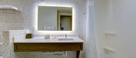 Un baño con lavamanos blanco, espejo y cortina de ducha.