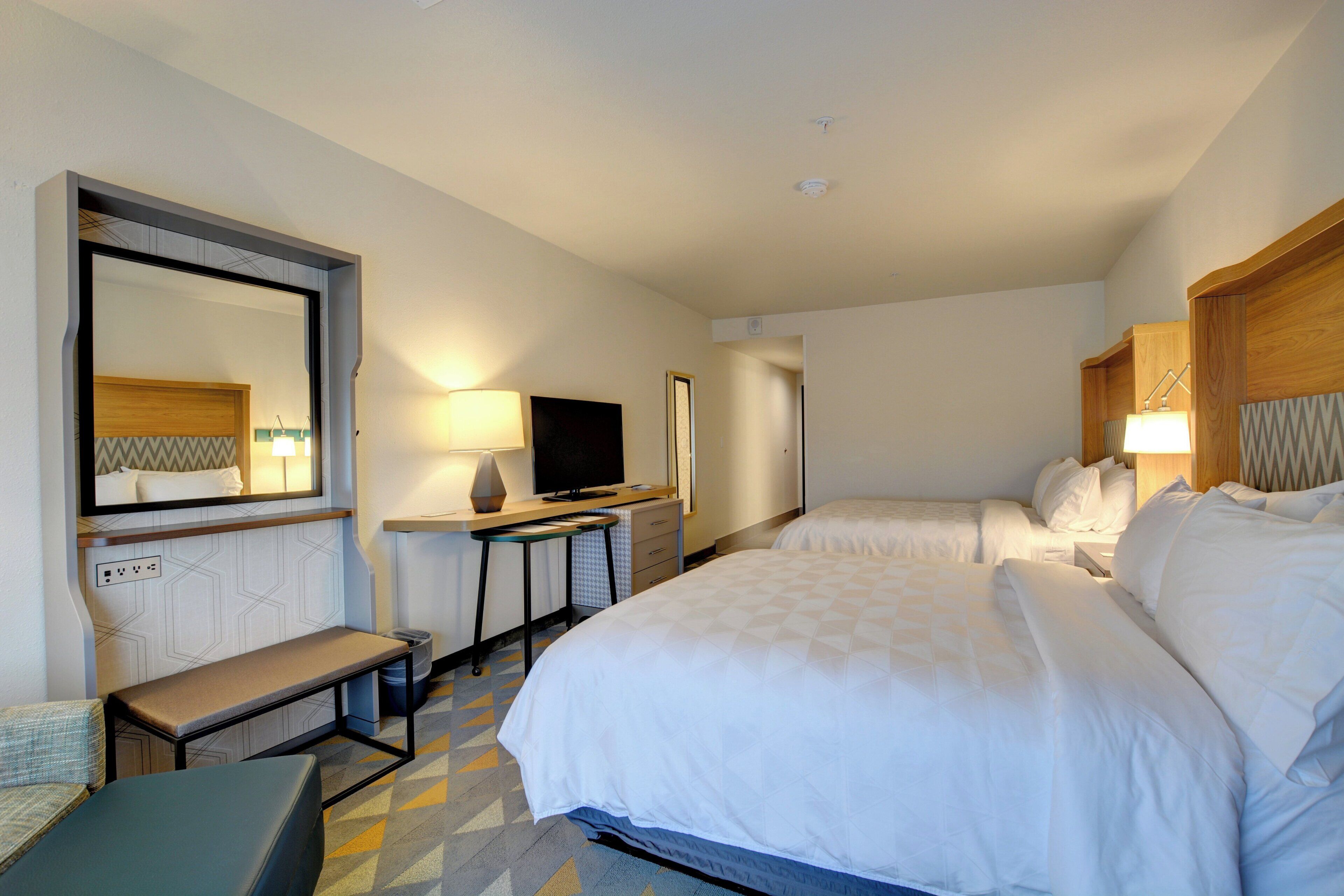 Een hotelkamer met een bed, bureau, televisie en spiegel.