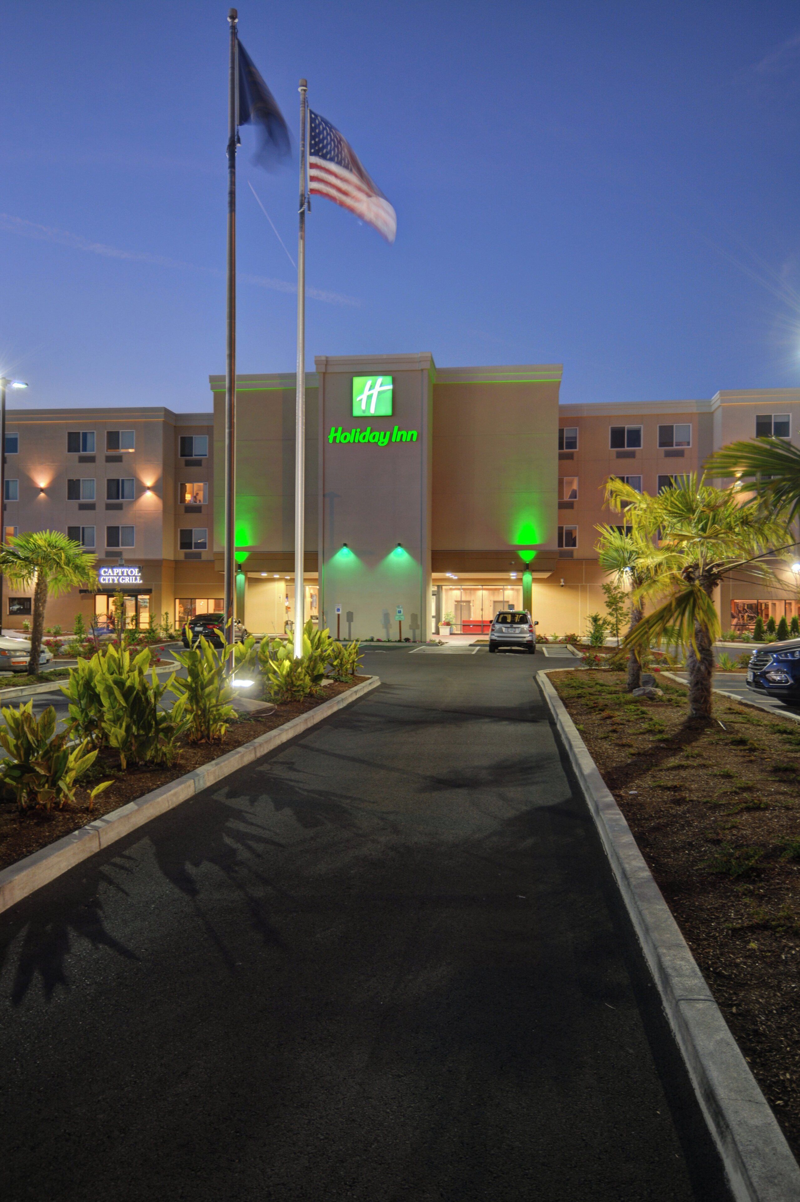 A Holiday Inn hotel with a flagpole, a well-lit entrance, and a parking lot.