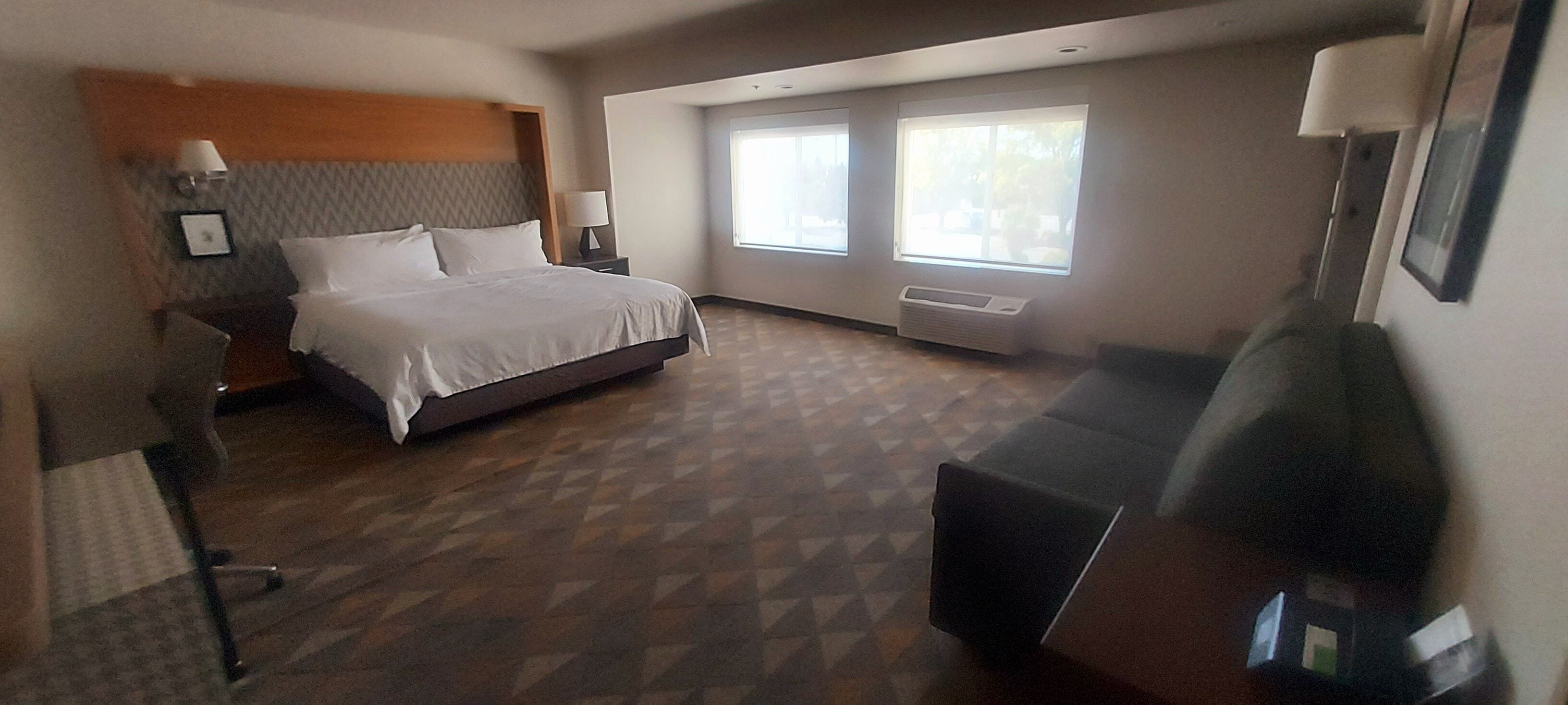 A hotel room with a bed, bedside table, lamp, and a large window.