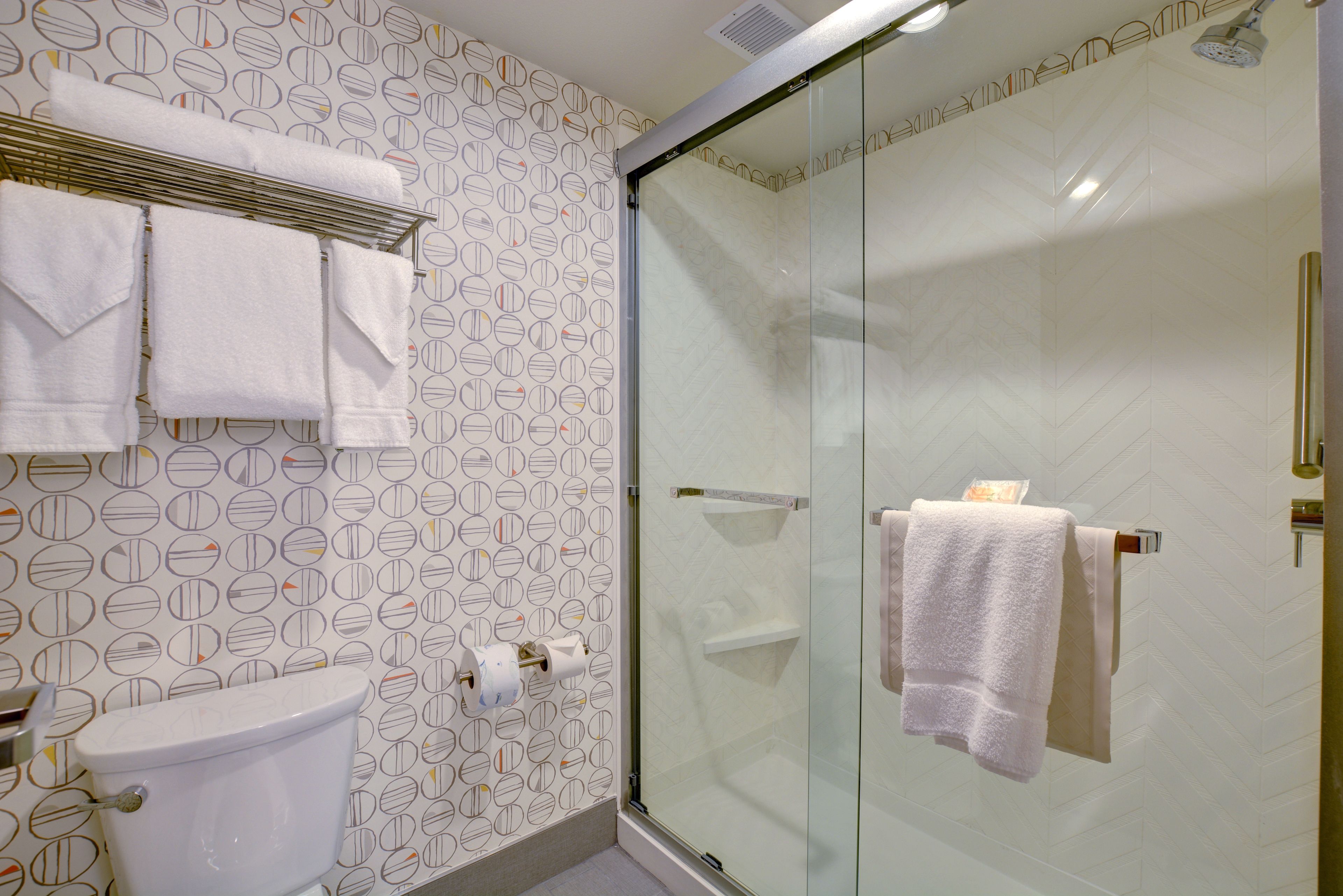 A bathroom with a toilet, a glass shower enclosure, and towels on a rack.