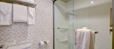 A bathroom with a toilet, a glass shower enclosure, and towels on a rack.
