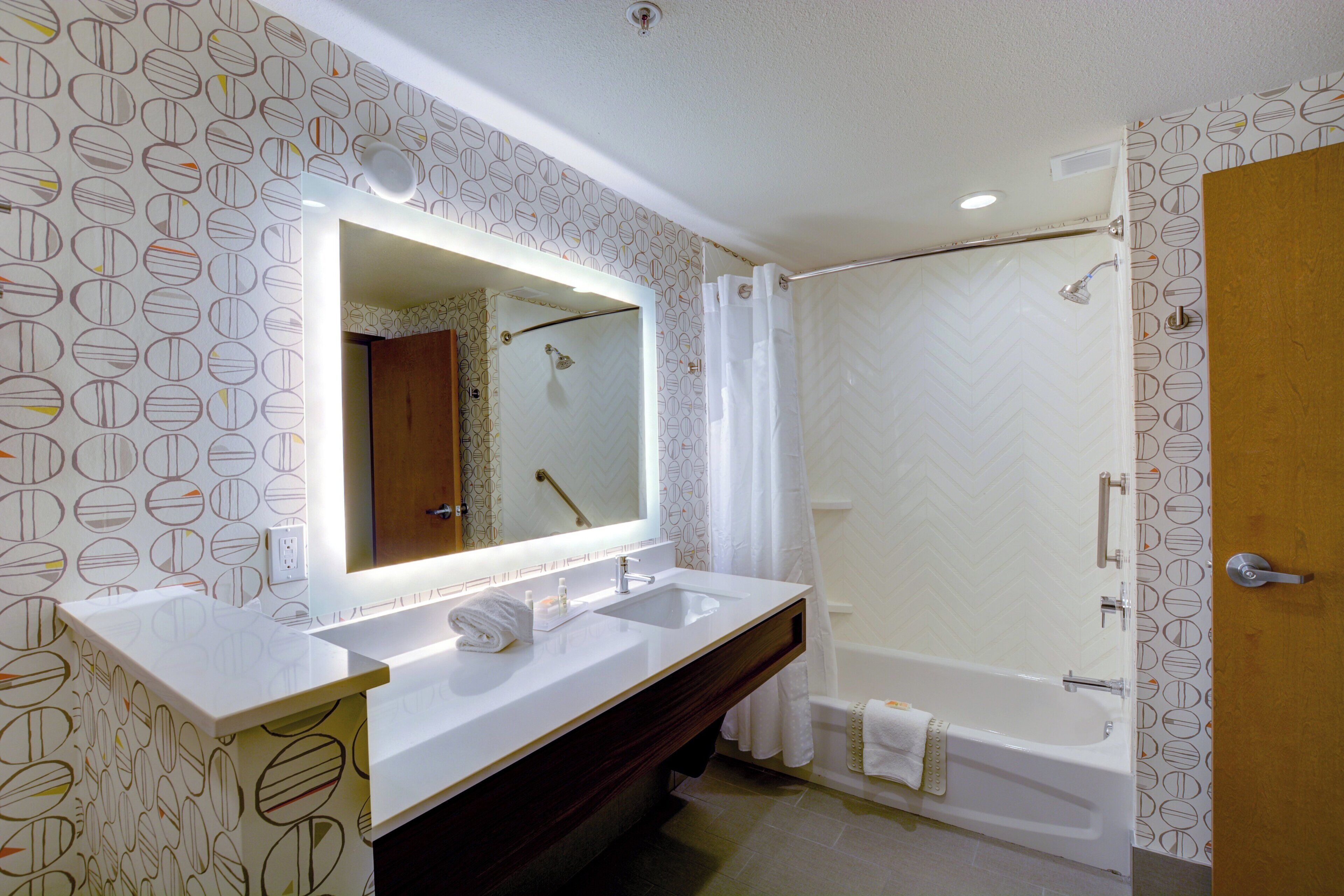Une salle de bain avec un grand miroir, deux lavabos, une douche et une porte.