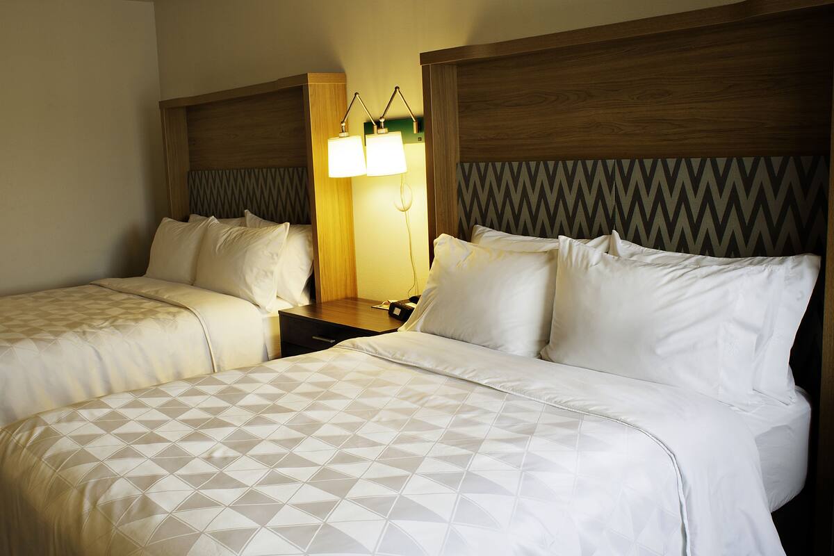 A hotel room with two beds, a nightstand, and a wall-mounted lamp.