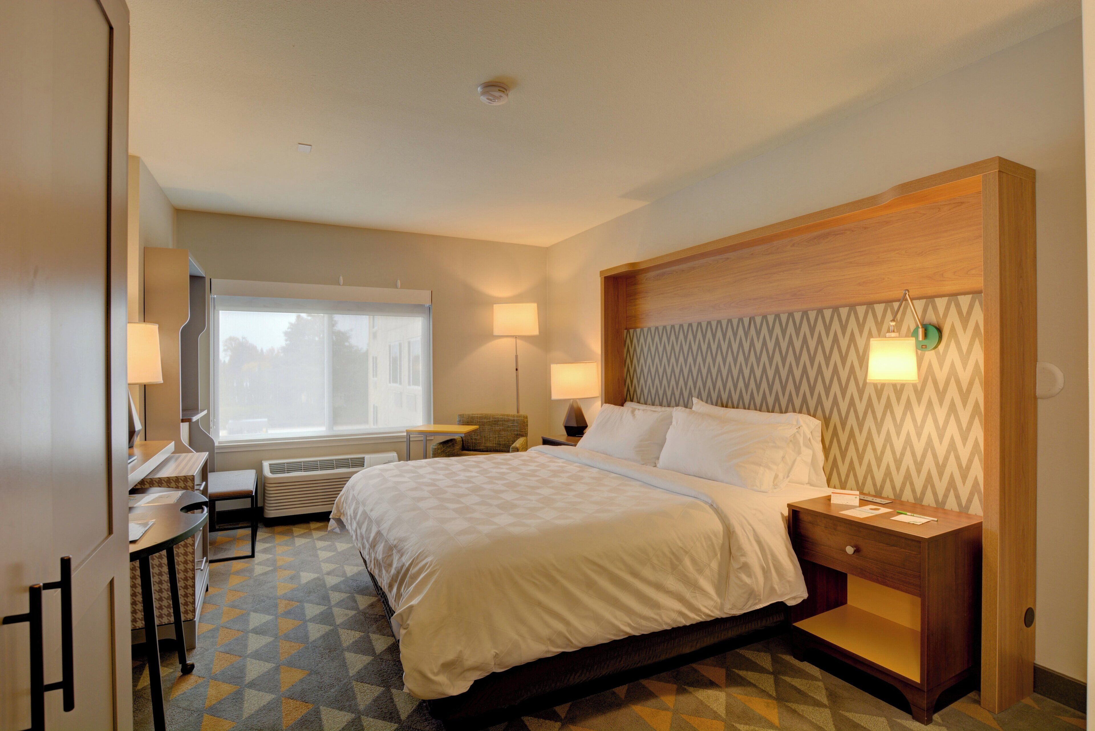 A hotel room with a bed, bedside tables, a desk, and a chair.