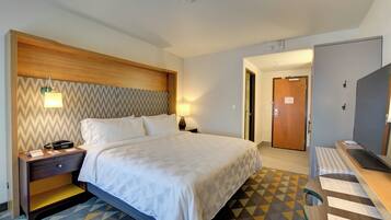 A hotel room with a bed, a nightstand, a desk, and a door.