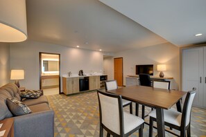 Ein Hotelzimmer mit Sofa, Esstisch, Stühlen, einer Küchenzeile und einem Badezimmer.