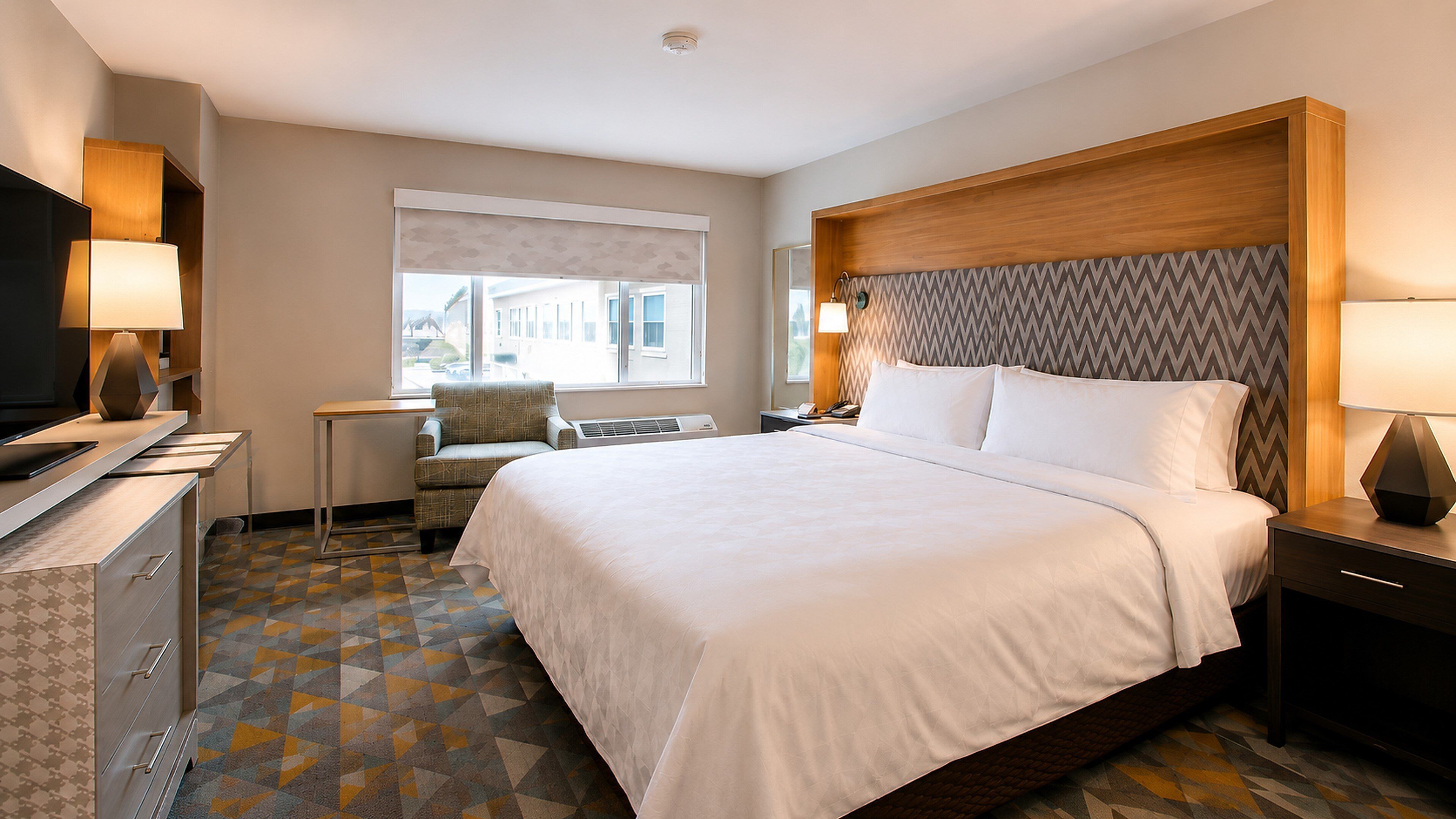 Une chambre d’hôtel avec un grand lit, des tables de chevet, un bureau et un téléviseur.