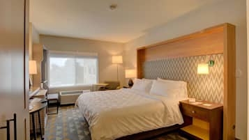 Een hotelkamer met een bed, nachtkastje, lamp, bureau, stoel en een raam.