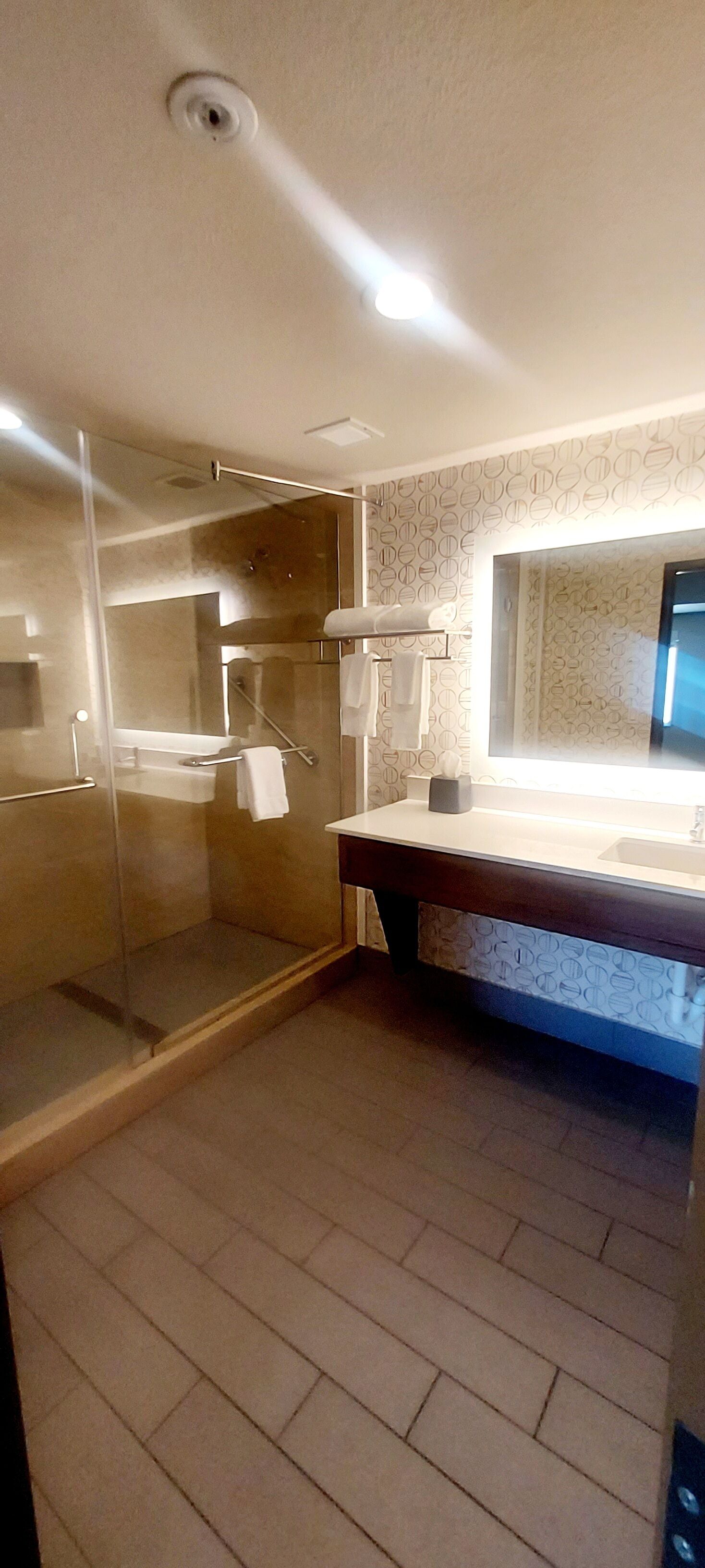 Un baño moderno con cabina de ducha de vidrio, lavamanos con espejo y azulejos decorativos.