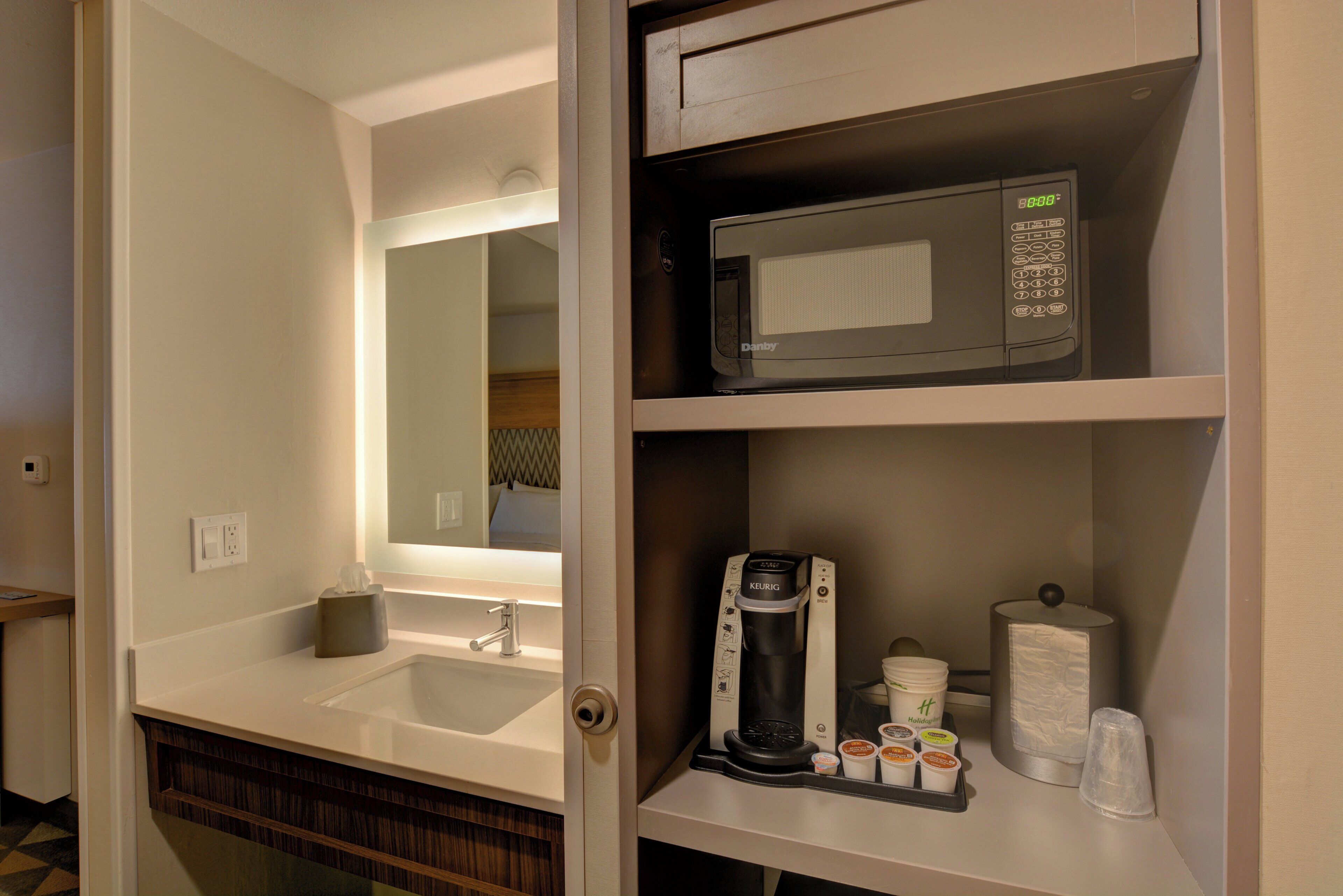 A hotel bathroom with a sink, mirror, microwave, and a coffee maker.