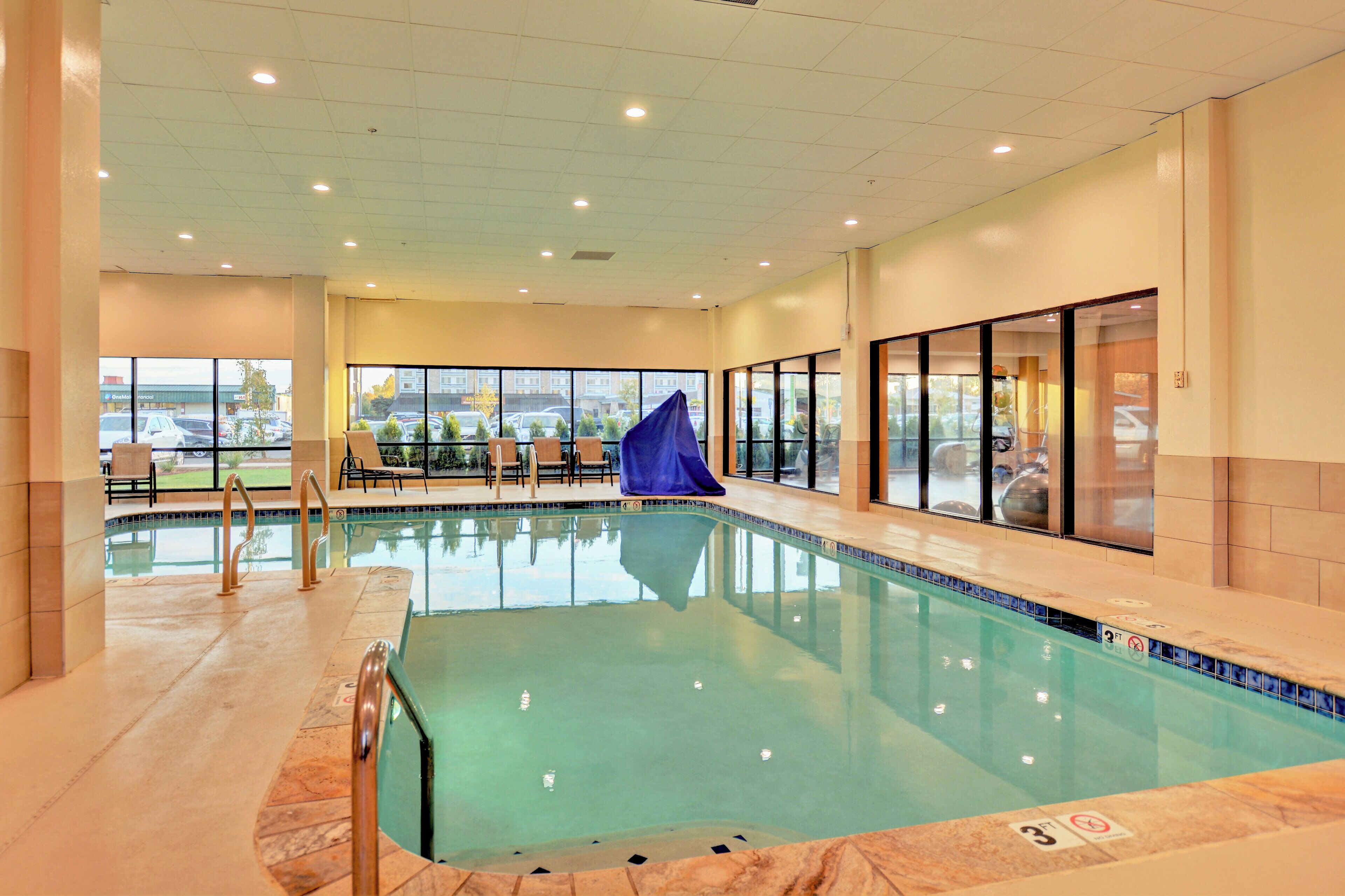 An indoor swimming pool with clear glass walls, a tiled floor, and a blue slide.