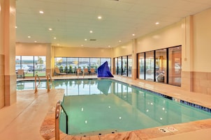An indoor swimming pool with clear glass walls, a blue slide, and a view of the outside parking area.