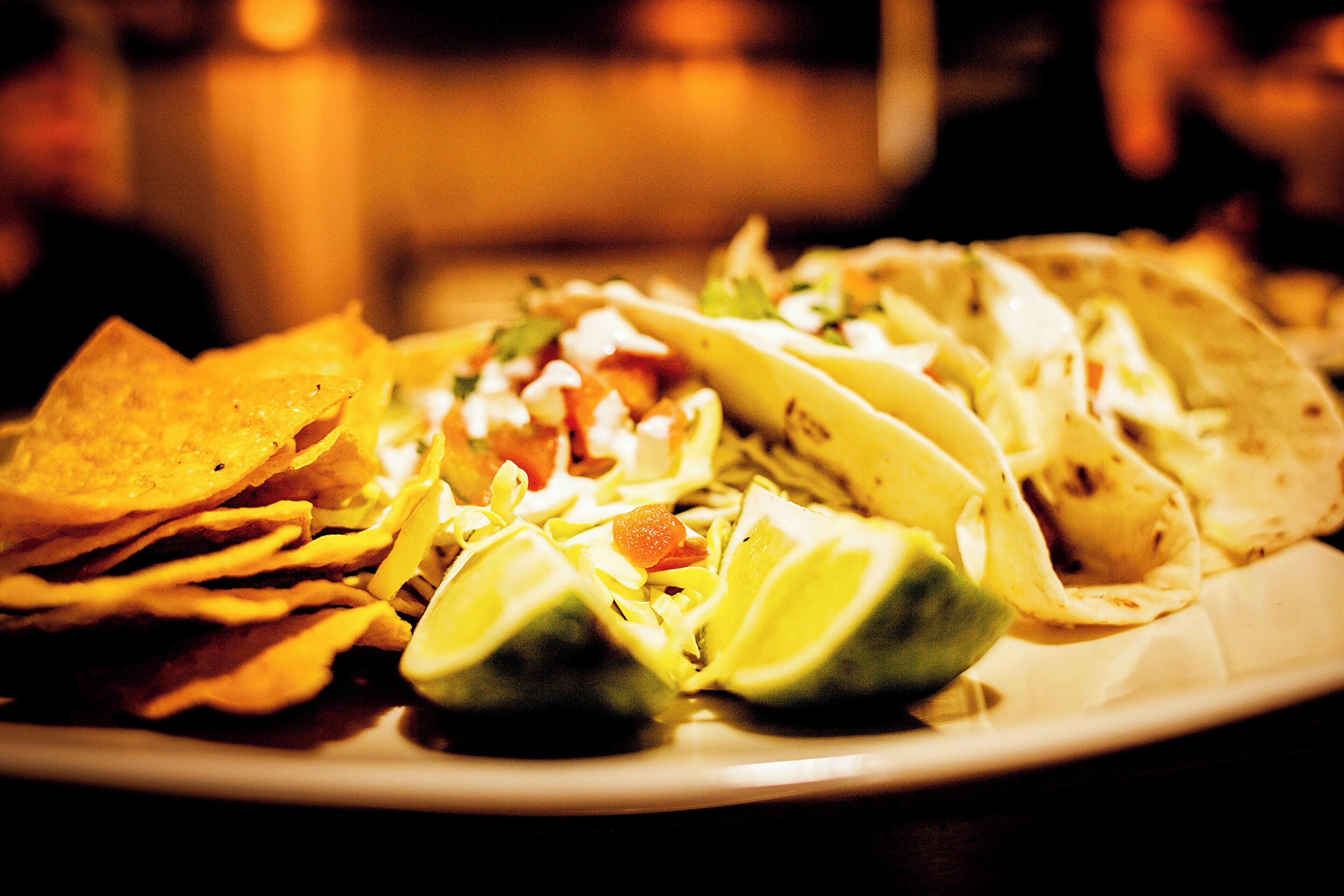 Een bord met taco's, chips en partjes limoen.