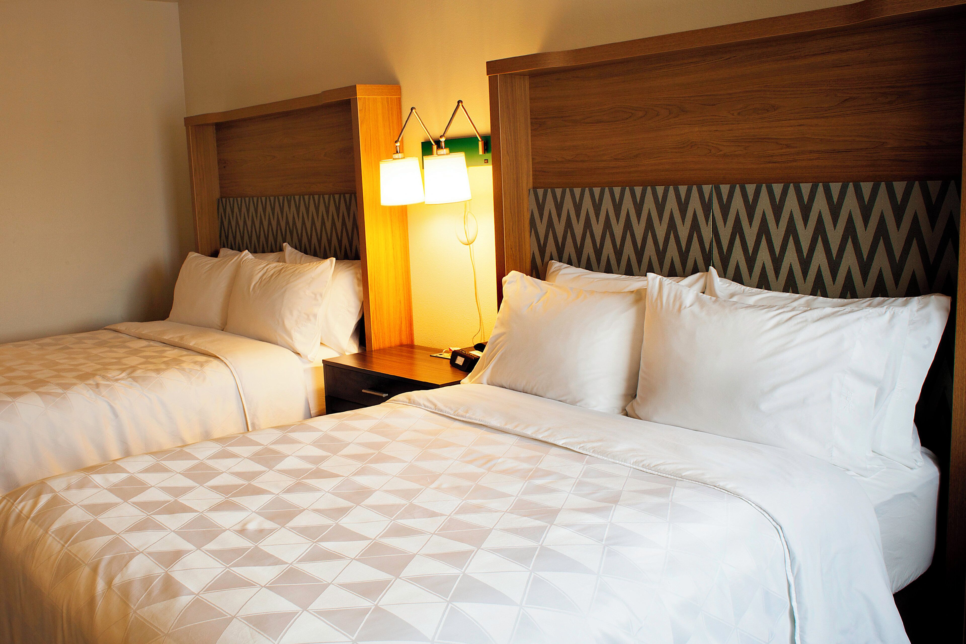 A hotel room with two beds, a nightstand, and a lamp.