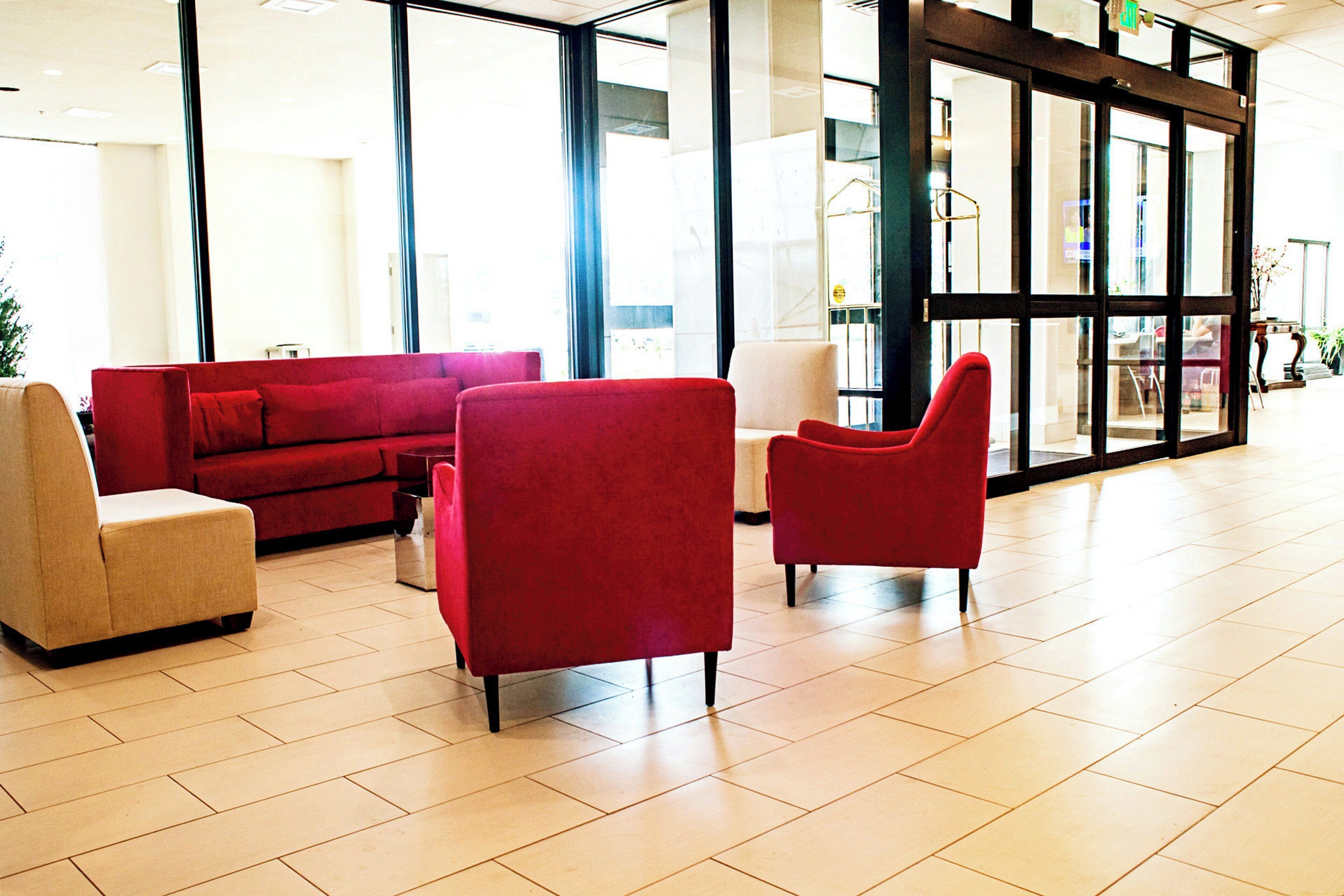 Un hall con un sofá rojo, un sillón beige y otro sillón rojo.