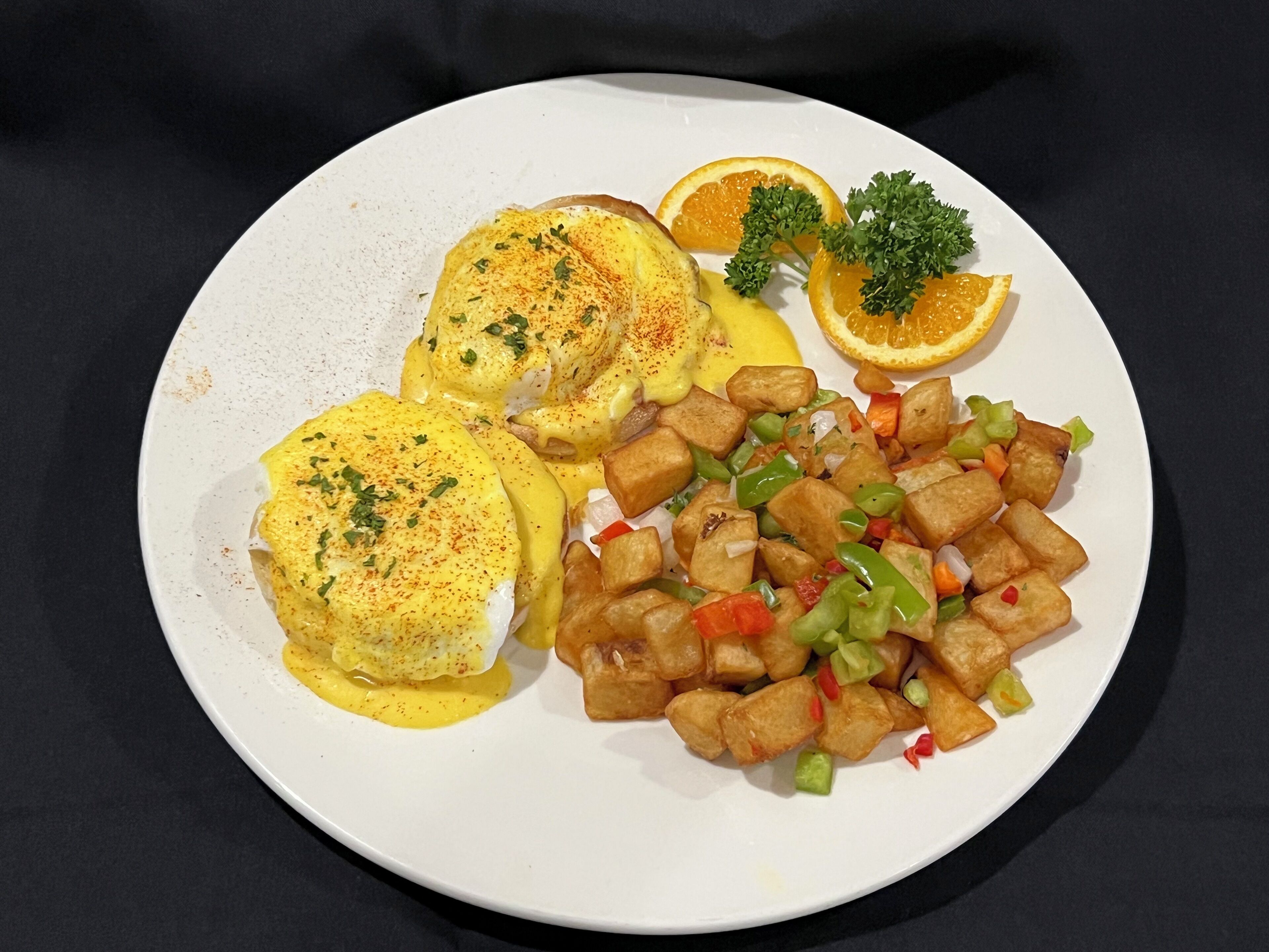 Um prato com ovos benedict, batatas assadas e fatias de laranja.
