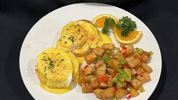 Um prato com ovos benedict, batatas assadas e fatias de laranja.