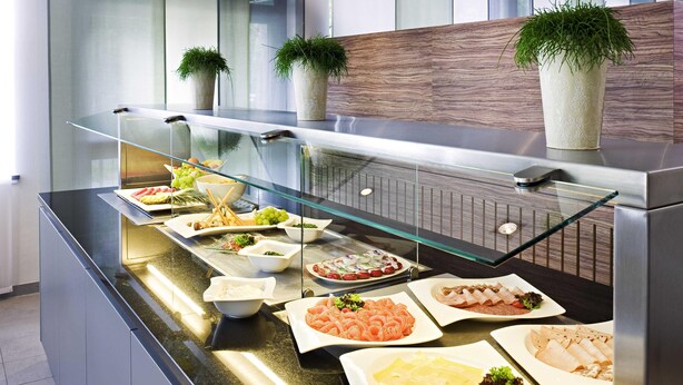 Een buffet met diverse gerechten, waaronder zeevruchten, salades en desserts, gepresenteerd op een glazen toonbank met een modern ontwerp.