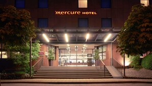 Een hotelentree met een bord waarop 'Mercure Hotel' staat, een trap die naar de ingang leidt, en een goed verlichte gevel.
