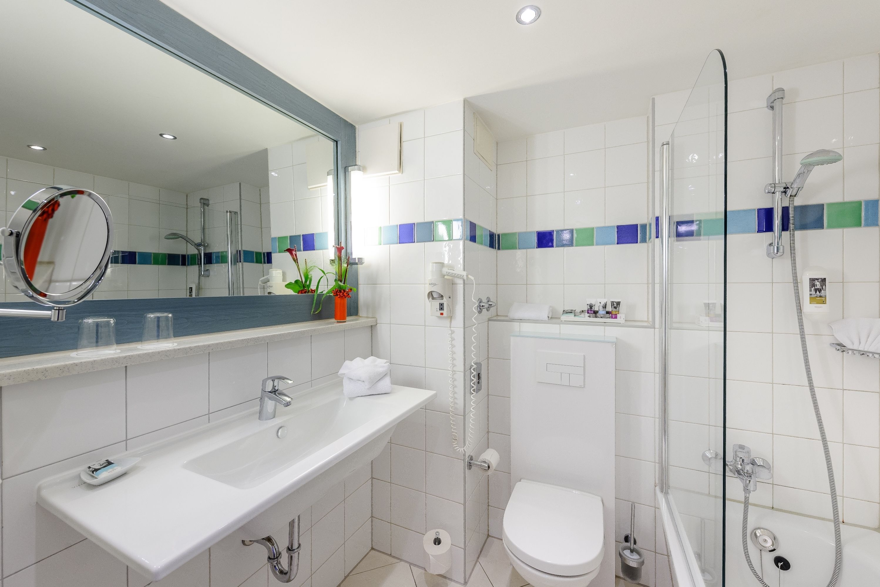 Ein modernes Badezimmer mit Waschbecken, Toilette, Dusche mit Glastür und Spiegel mit rundem Rahmen.