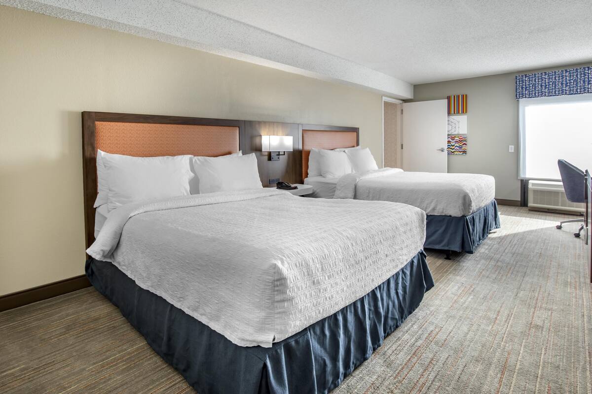 Quarto de hotel com duas camas, uma escrivaninha e uma cadeira.
