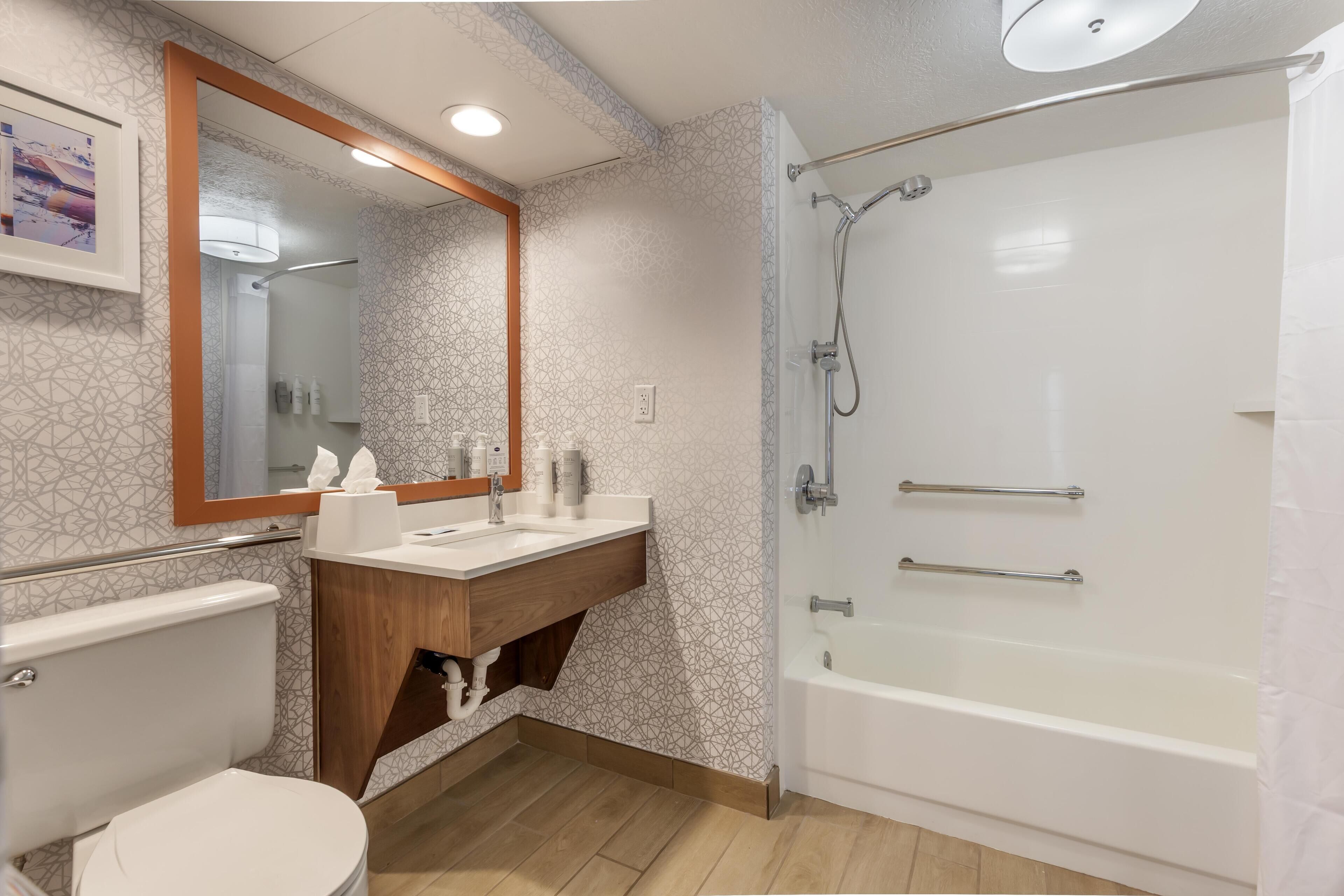 A modern bathroom with a toilet, vanity, mirror, shower, and bathtub.