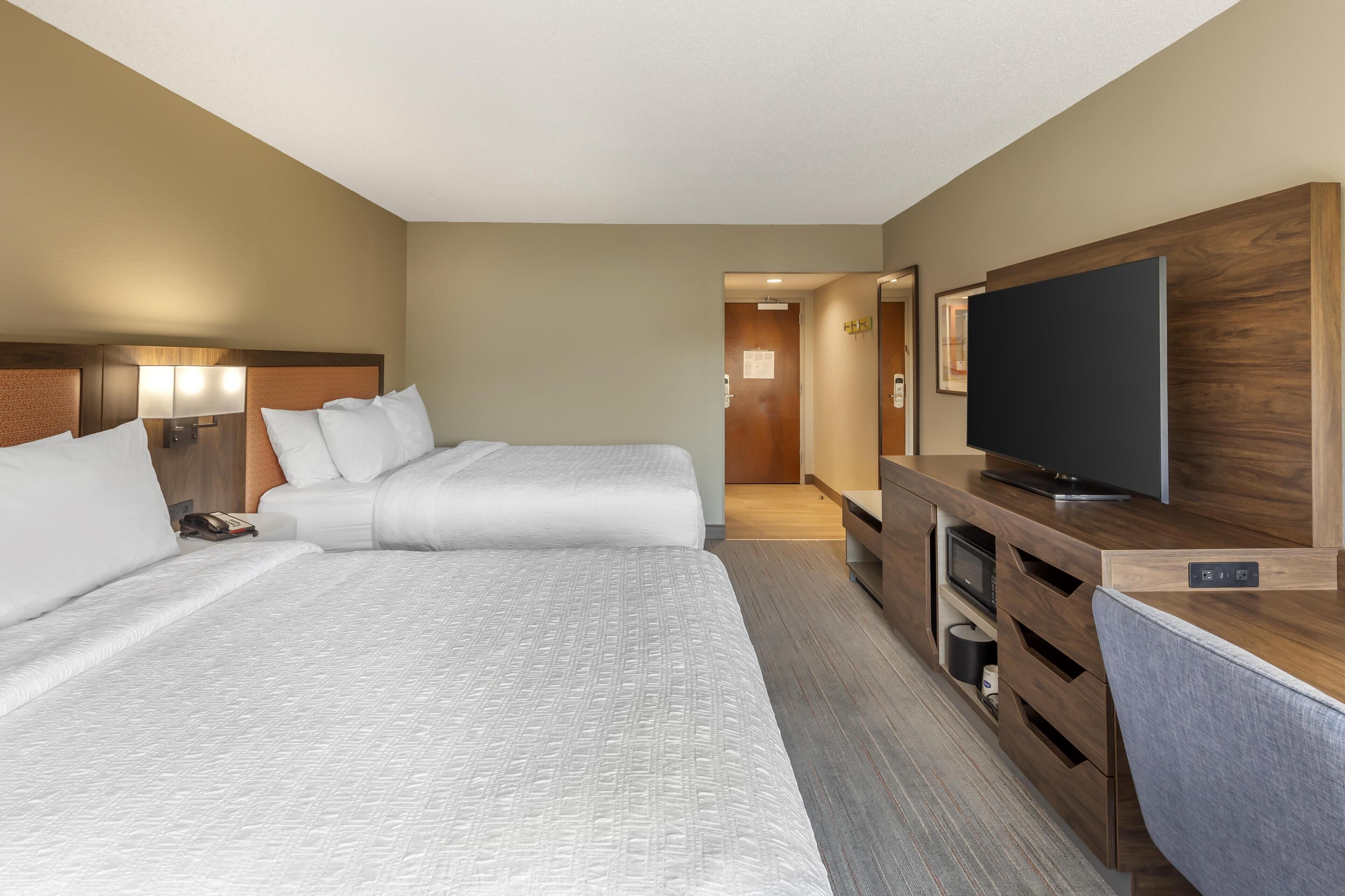 A hotel room with two beds, a TV, and a wooden desk.