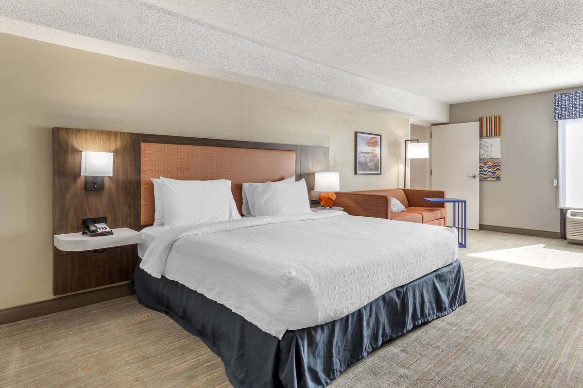 Quarto de hotel com cama grande, mesas de cabeceira, escrivaninha e uma cadeira.
