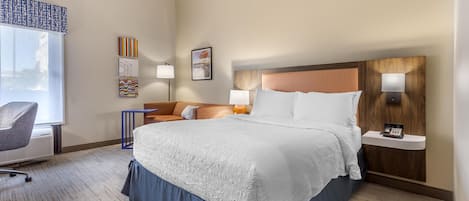 Habitación de hotel con una cama grande, un escritorio con silla, una mesita de noche con lámpara y obras de arte en las paredes.