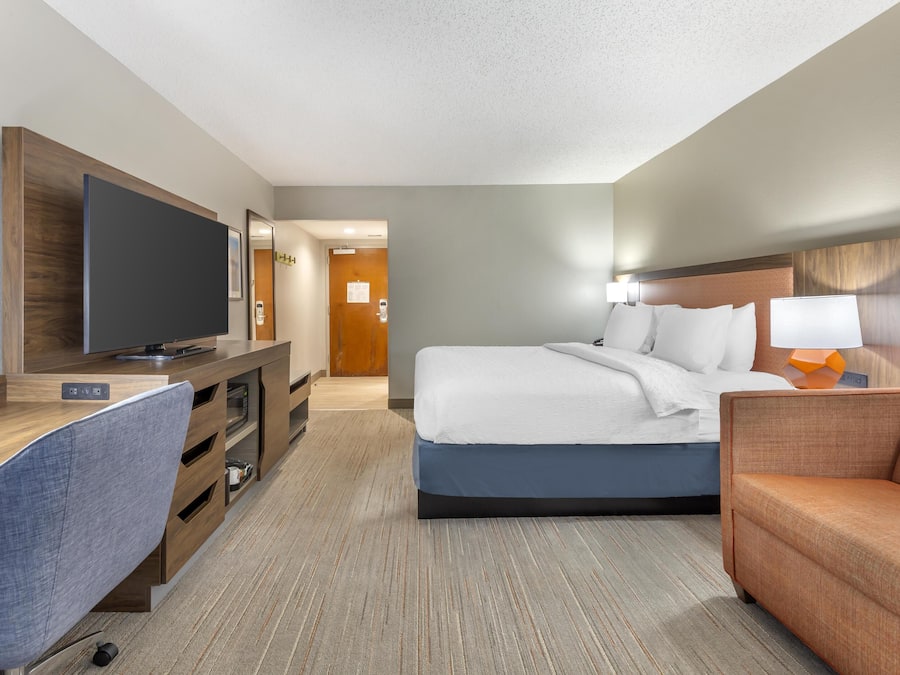 A hotel room with a bed, a desk with a chair, a television, and a sofa.
