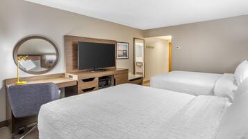 Quarto de hotel com duas camas, uma escrivaninha, televisão de tela plana, espelho e um pequeno espaço para sentar.