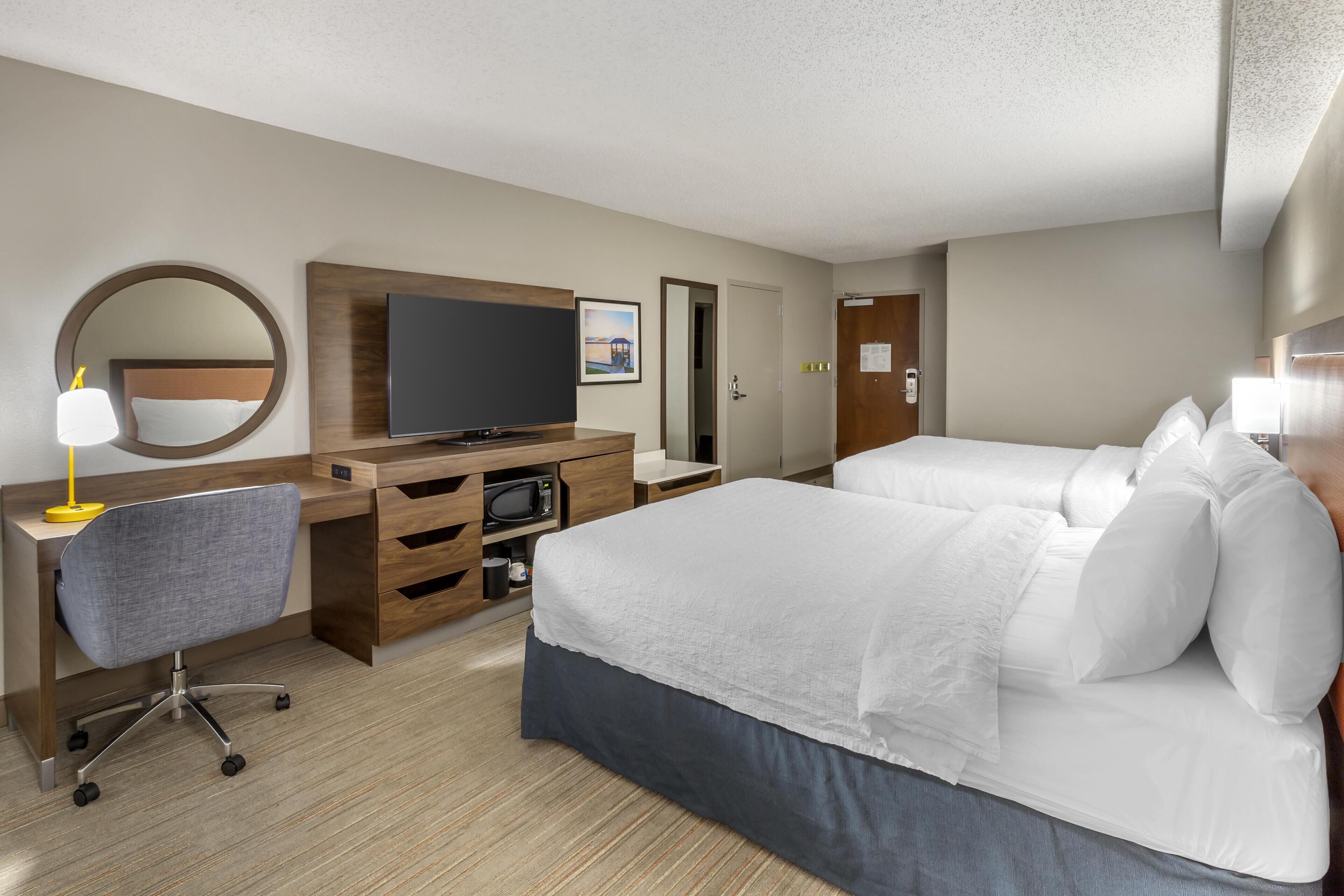 Une chambre d’hôtel comprenant un lit, un bureau avec une chaise, une télévision et un miroir.