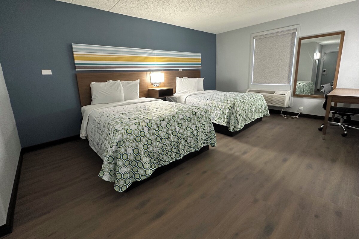 A hotel room with two beds, a desk, a chair, a large mirror, and a ceiling light.