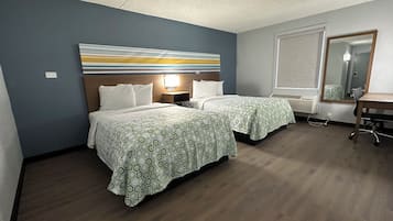 A hotel room with two beds, a desk, a chair, a large mirror, and a wall-mounted light fixture.