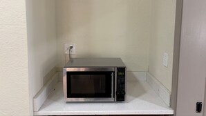 A microwave on a white countertop in a corner with a textured wall and a door frame. - HomeTowne Studios by Red Roof Richmond, VA - W Broad St (Richmond)