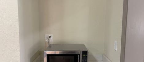 A microwave on a white countertop in a corner with a textured wall and a door frame.