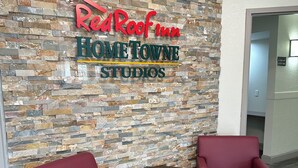 A reception area with a stone wall, two red chairs, and a small round table. - HomeTowne Studios by Red Roof Richmond, VA - W Broad St (Richmond)