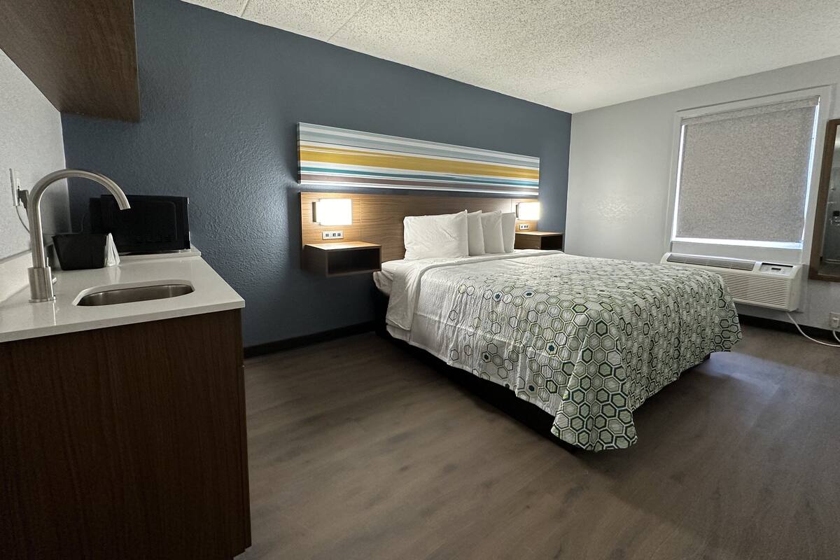 A hotel room with a bed, bedside table, nightstand, and a window with a view.