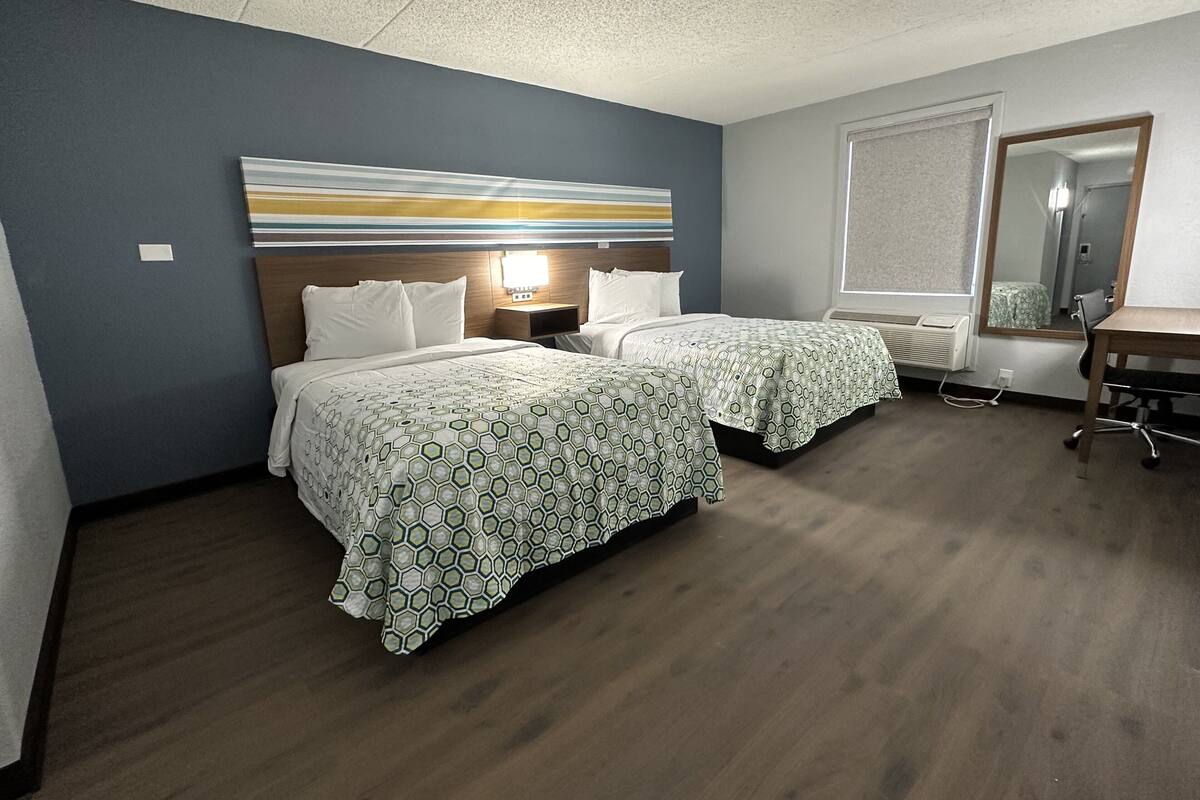 A hotel room with two beds, a desk, a chair, a large mirror, and a ceiling light.