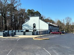A parking lot with a building that has a modern design, a small tree, and a red car parked.