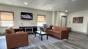 A spacious room with a brown leather sofa, a coffee table, and a flat-screen TV mounted on the wall. - HomeTowne Studios by Red Roof Richmond, VA - W Broad St (Richmond)