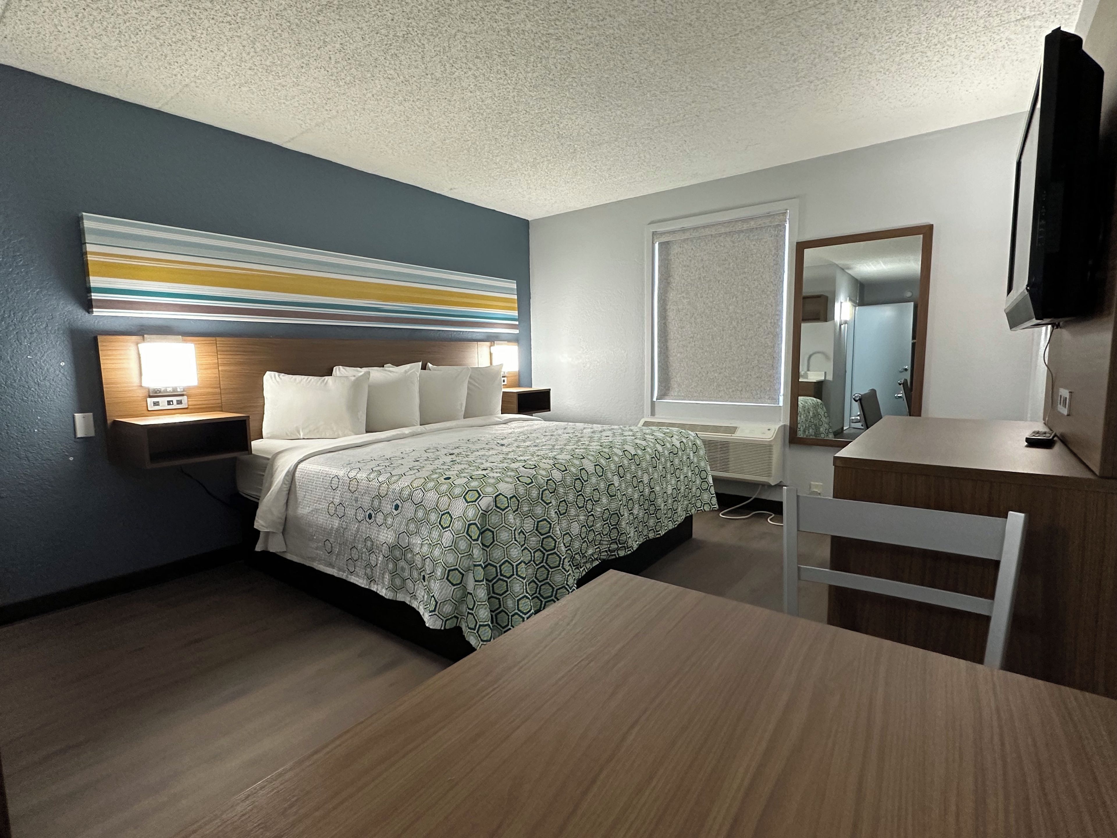 Una habitación de hotel con cama, mesita de noche, escritorio, silla y televisor.