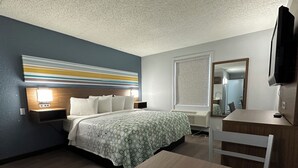 A hotel room with a bed, bedside table, desk, chair, and a television. - HomeTowne Studios by Red Roof Richmond, VA - W Broad St (Richmond)