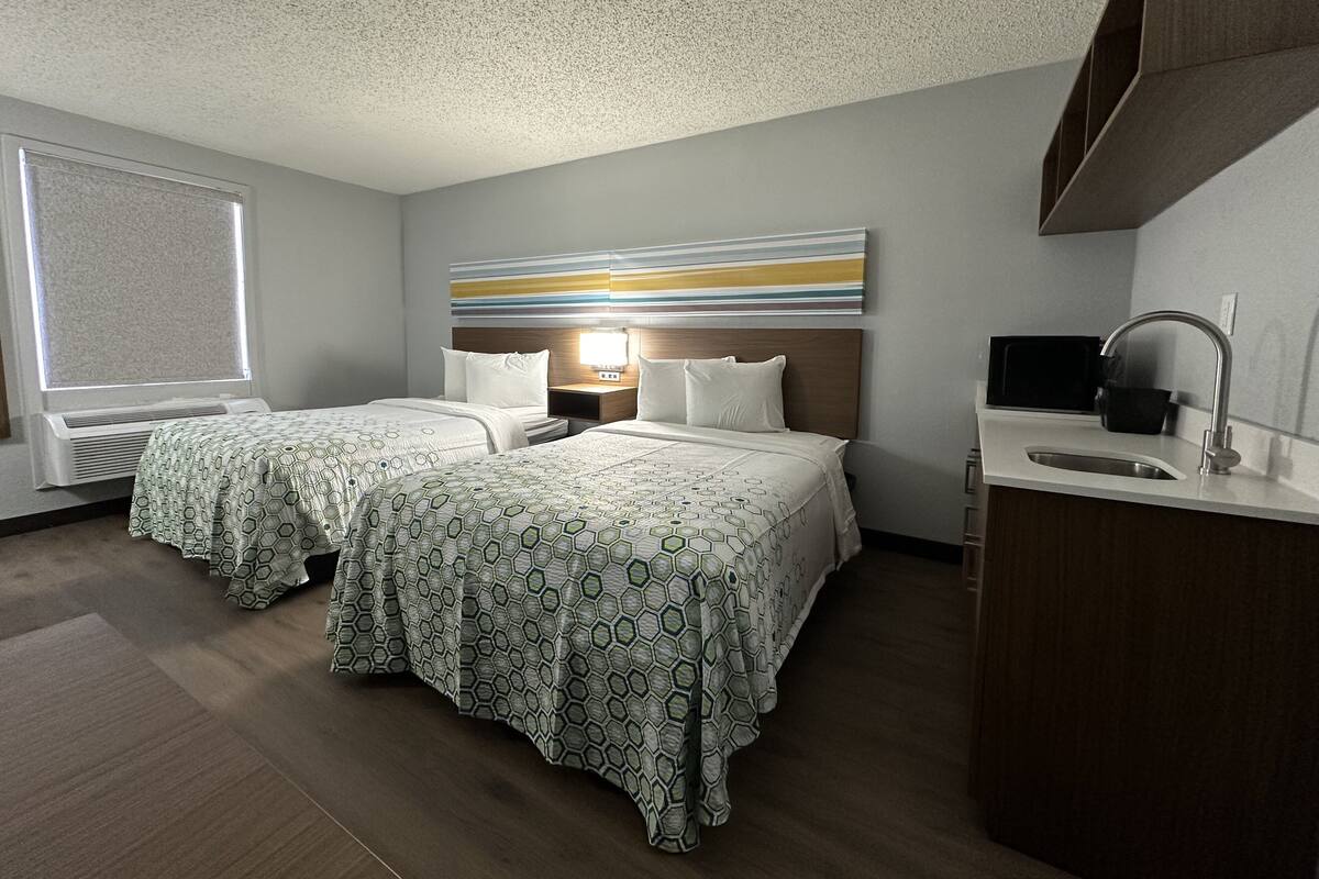 A hotel room with two beds, a large window, a modern bathroom, and a decorative wall piece.